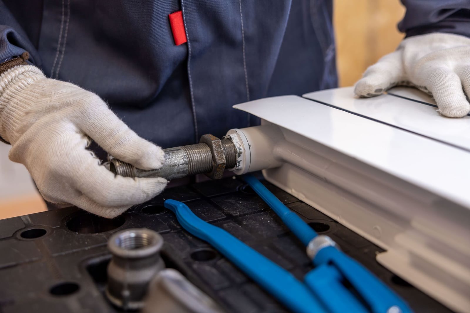 A heating engineer in gloves working on a radiator valve with pipe wrenches laid out